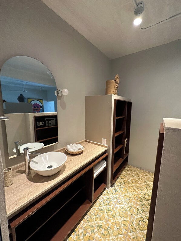 A bathroom with a white sink, a mirror, a wooden vanity, a shelf with a decorative item, and patterned floor tiles.
