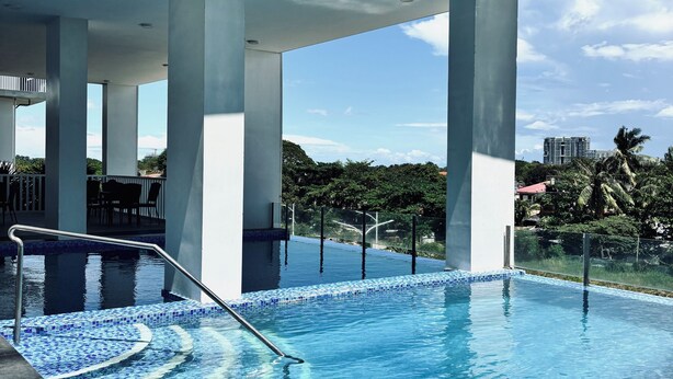 A modern pool area with clear blue water, a tiled deck, and a view of distant buildings and greenery.