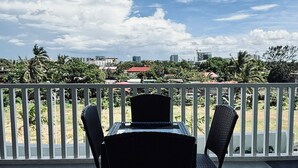 An outdoor patio with a table and chairs, a white railing, and a view of a cityscape with buildings and trees.