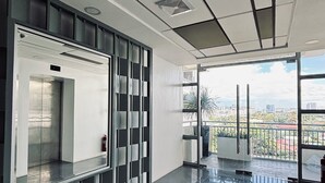 A modern interior with a glass elevator, a view of the city, and a balcony with a railing.