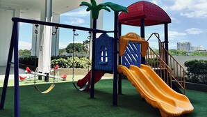 A playground with swings and slides, set against a building with balconies.