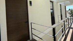 A modern building with a large wooden door, a balcony with a glass railing, and a clear sky. - Apartment with Private Rooftop. Start your adventure here at Zefira - 2BR. (Mérida)