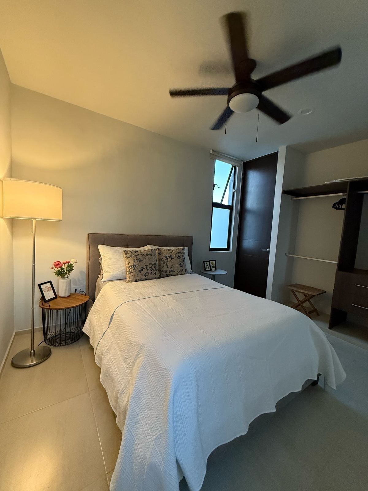 Un dormitorio con una cama, una mesita de noche con lámpara, un ventilador de techo y un armario.