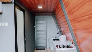 A compact kitchen with a modern design, featuring a built-in stove, a coffee maker, and a small countertop. - Dieng Ceria By Travelink (Dieng Kulon)