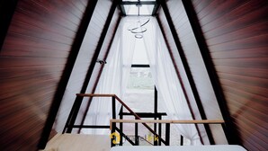 A room with a sloped ceiling, wooden paneling, a metal railing, and a view through a window. - Dieng Ceria By Travelink (Dieng Kulon)