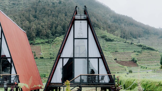 A modern, triangular-roofed building with a glass facade, situated in a lush, terraced landscape. - Dieng Ceria By Travelink (Dieng Kulon)