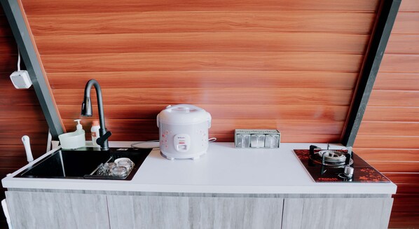 A compact kitchenette with a sink, a rice cooker, a coffee maker, and a small electric stove.