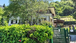A building with a white facade, surrounded by lush greenery and a green fence. - Nel Castagneto by Interhome (Varenna)