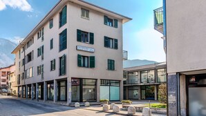 A multi-story building with a sign for "Studio Tecnico Legale Etrusque C.L." The building has multiple windows with green shutters, a ground floor entrance, and a visible parking area.