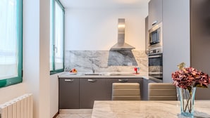 A modern kitchen with a marble backsplash, a built-in stove, and a dining area with a marble table and chairs.