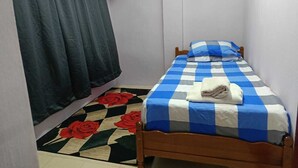 A small, single-bed room with a checkered bedspread, a dark curtain, a floral-patterned rug, and a small wall decoration. - Homestay Budget Alor Setar (Jitra)