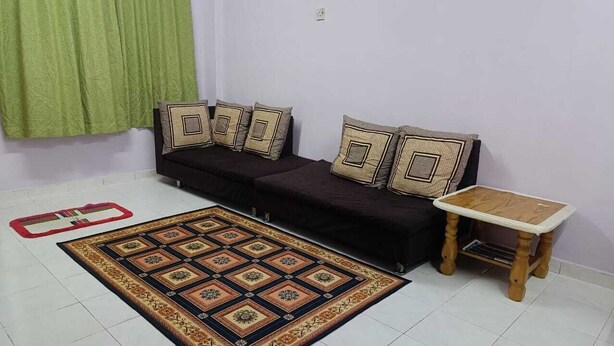 A living room with a black sofa, patterned cushions, a wooden table, and a decorative rug. - Homestay Budget Alor Setar (Jitra)