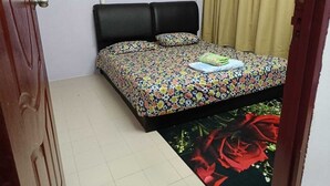 A bedroom with a bed, a floral bedspread, a green pillow, a white pillow, a black headboard, and a red rose design on the floor. - Homestay Budget Alor Setar (Jitra)