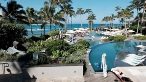 Et resortområde med swimmingpool, palmer, liggestole og udsigt over havet.