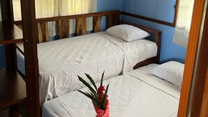 A room with two single beds, a wooden headboard, a window with sheer curtains, and a pink vase with flowers on the lower bed. - Costa Rica Getaway 2 (Jaco)