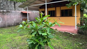 A building with a covered porch, a brick wall, and a grassy area with a plant in the foreground. - Costa Rica Getaway 2 (Jaco)