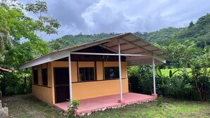 A small, single-story building with a yellow exterior and a red roof. It has a covered porch area and is surrounded by lush greenery and hills in the background. - Costa Rica Getaway 2 (Jaco)