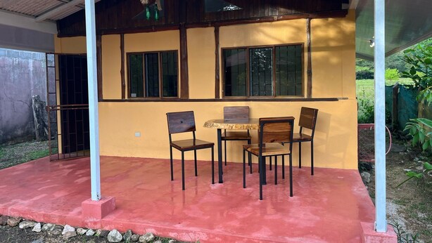 A covered patio area with a table and chairs, a wooden bench, and a metal railing. - Costa Rica Getaway 2 (Jaco)