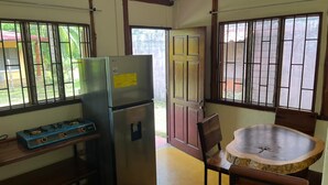 A compact kitchen with a refrigerator, a gas stove, a wooden dining table, and a window with bars. - Costa Rica Getaway 2 (Jaco)