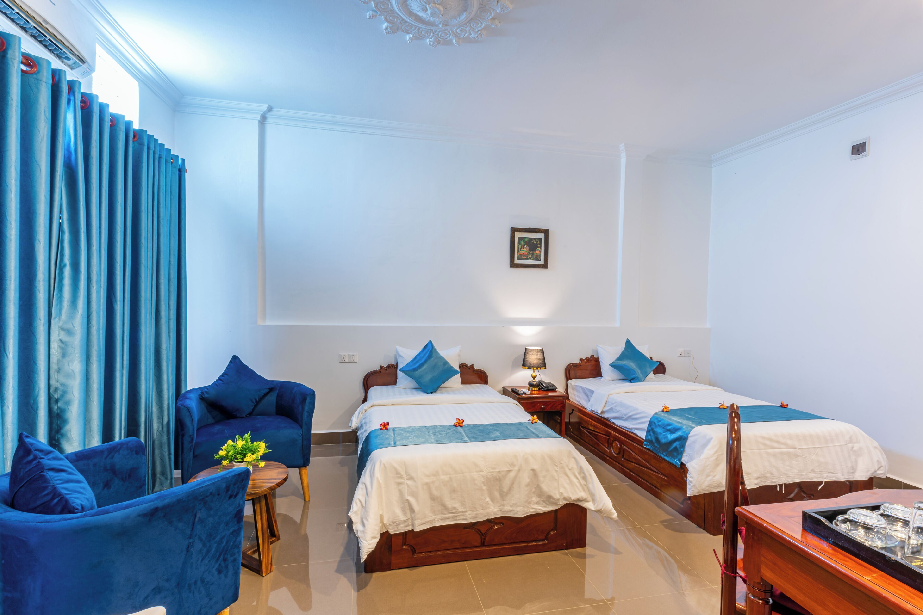 A hotel room with two beds, a sitting area with a chair, a small table with a plant, and a wooden side table with a tray.