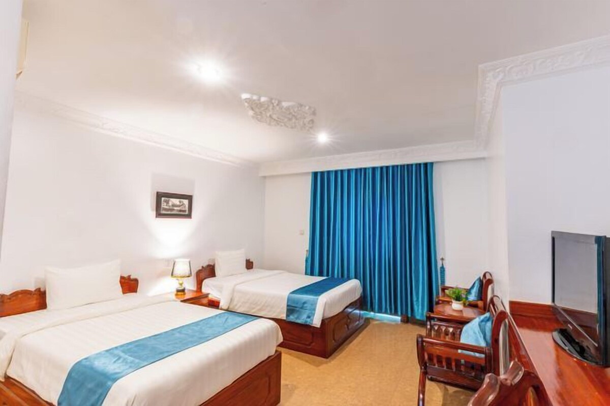 Une chambre d’hôtel avec deux lits, une télévision, un bureau et une fenêtre avec des rideaux.