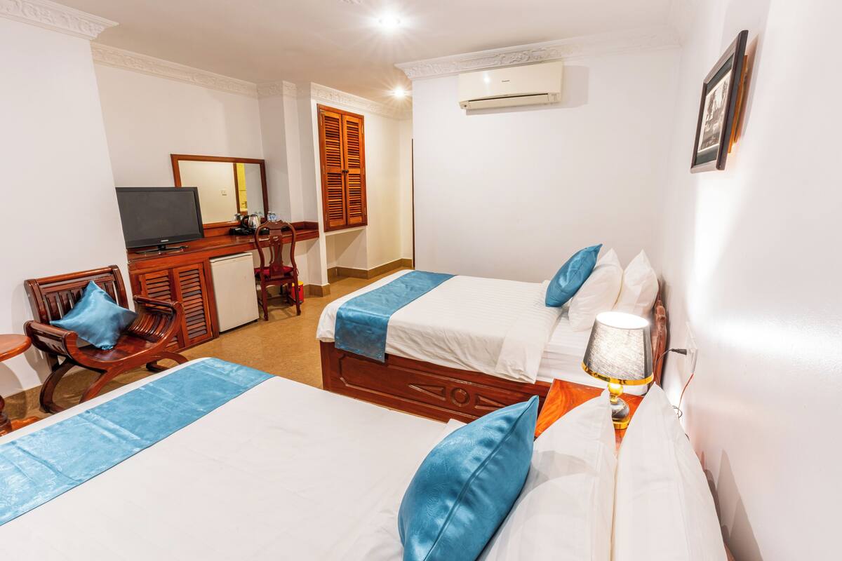 A hotel room with two beds, a desk, a chair, a television, and an air conditioning unit.