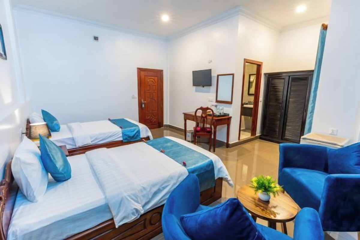 Une chambre d’hôtel avec deux lits, un bureau, une chaise et une petite table sur laquelle est posée une plante.