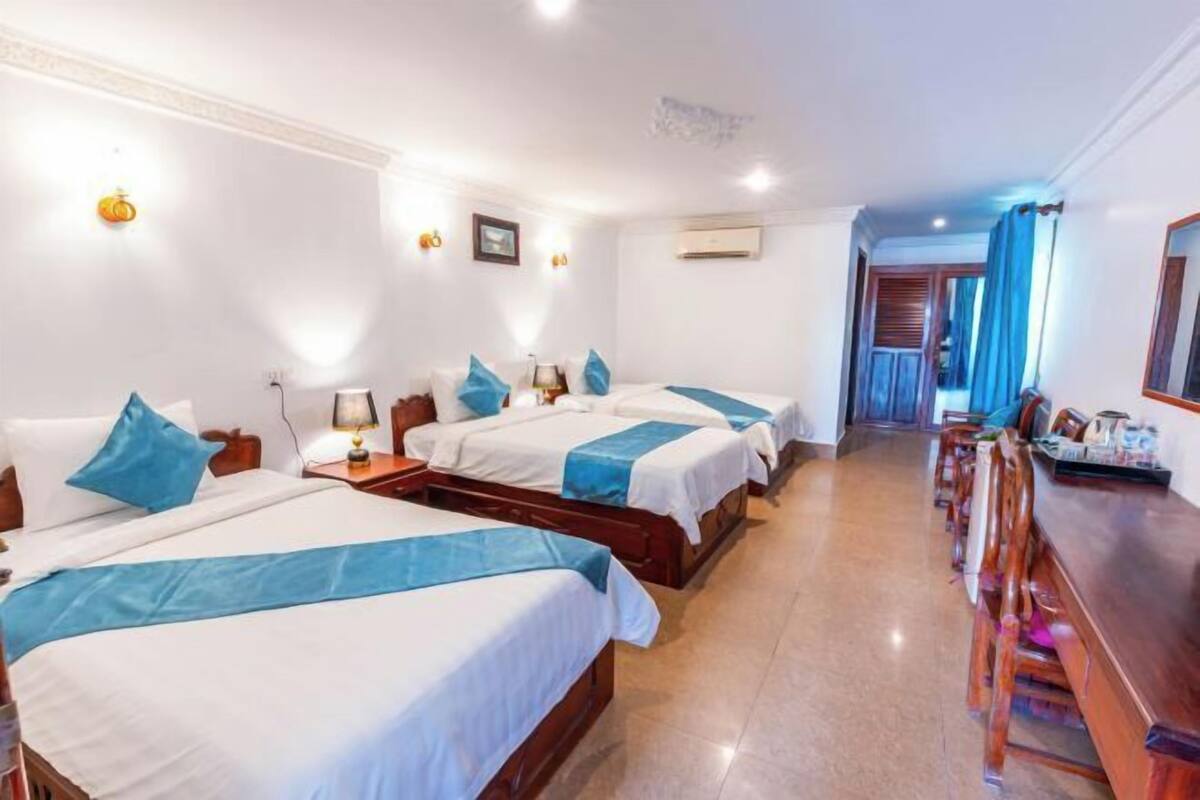 A hotel room with three beds, a wooden desk, and a view of the corridor.