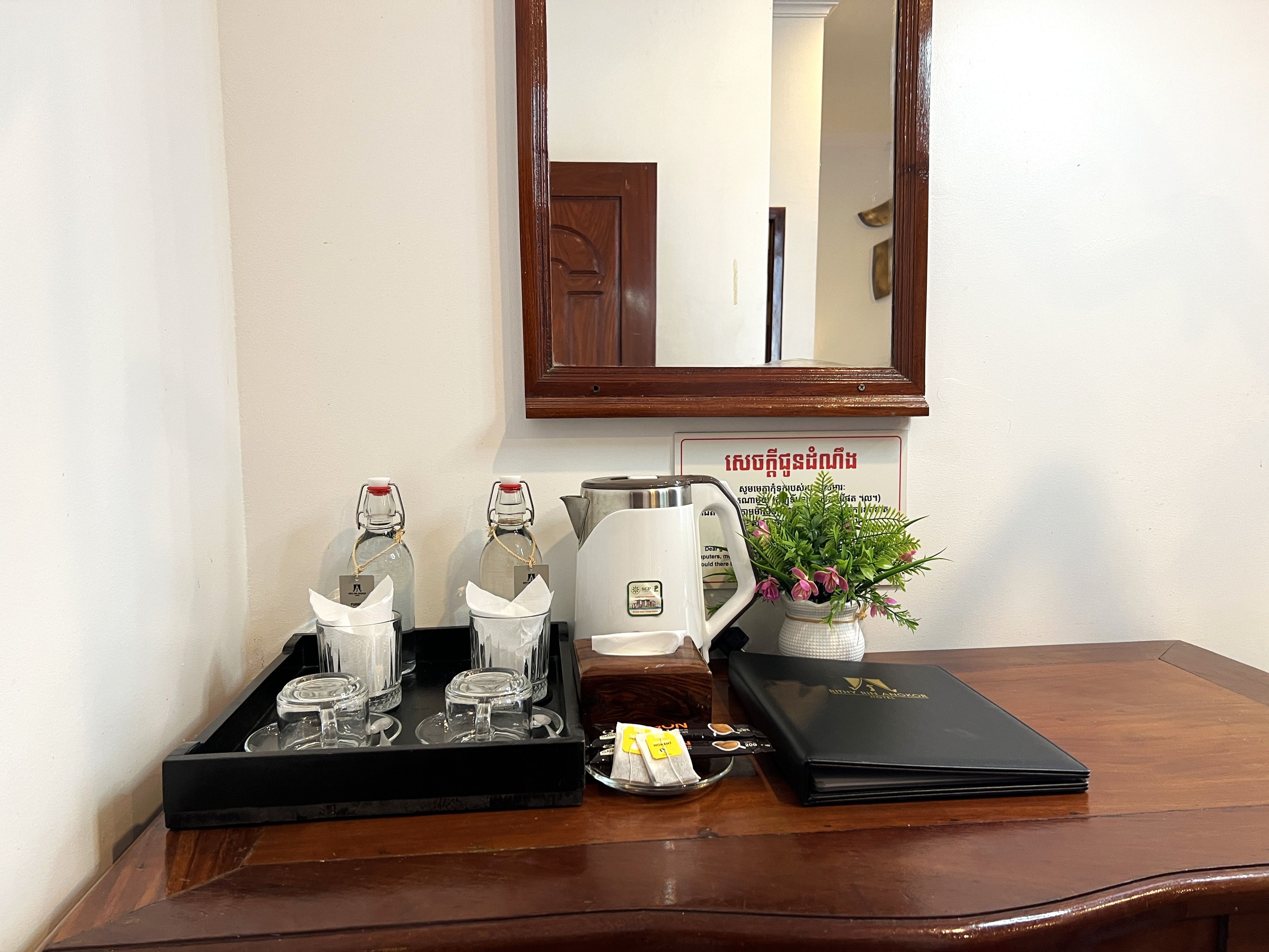 A wooden table with a tray holding glass bottles, a kettle, a small potted plant, a tea set, and a black folder.