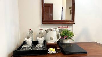 A wooden table with a tray holding glass bottles, a kettle, a small potted plant, a tea set, and a black folder.