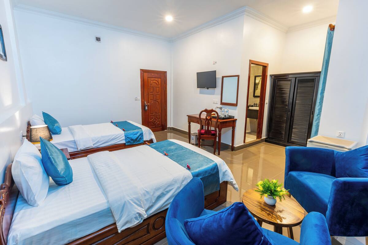 A hotel room with two beds, a desk, a chair, a TV, and a wardrobe.