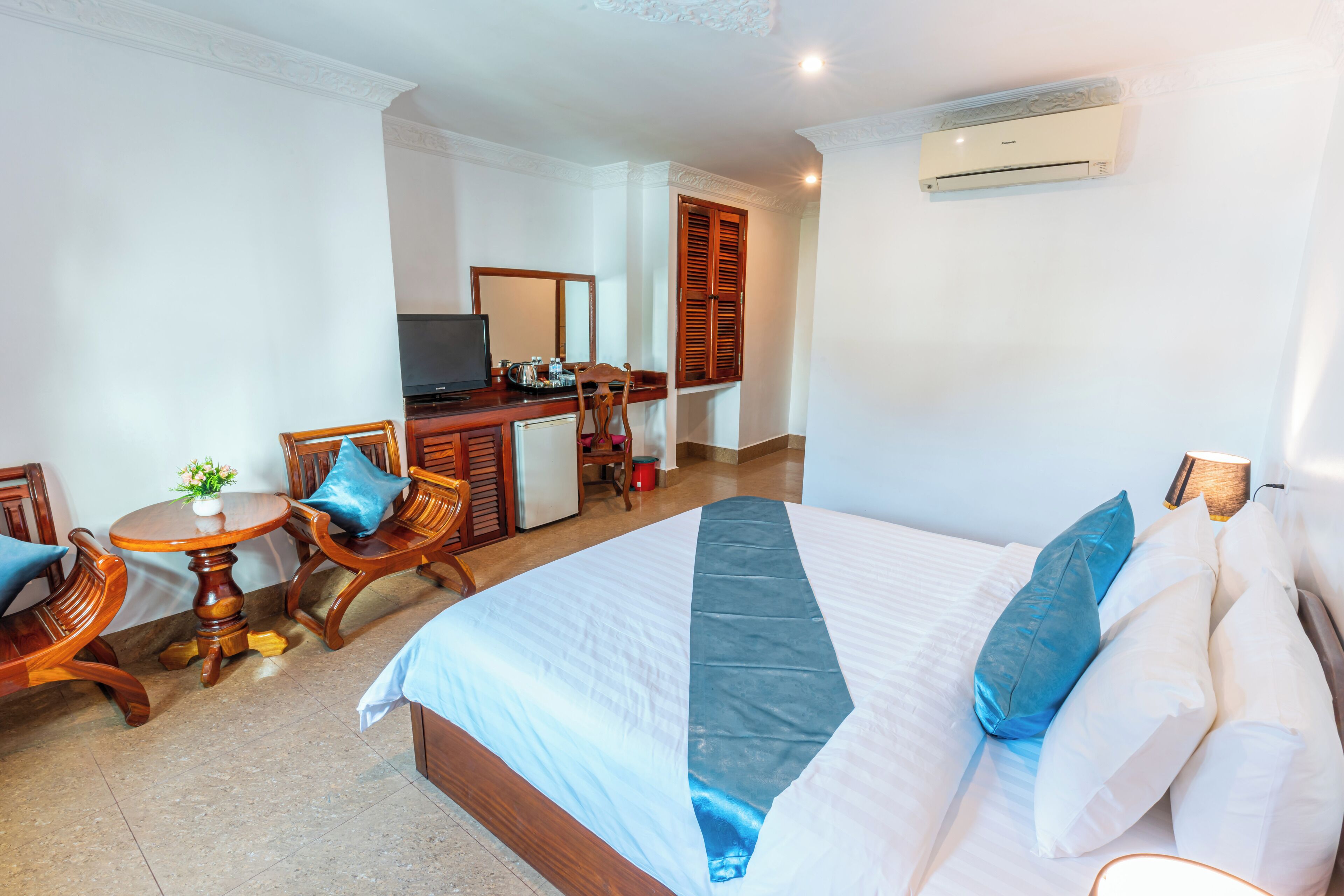 A hotel room with a bed, a desk, a chair, a television, and an air conditioning unit.