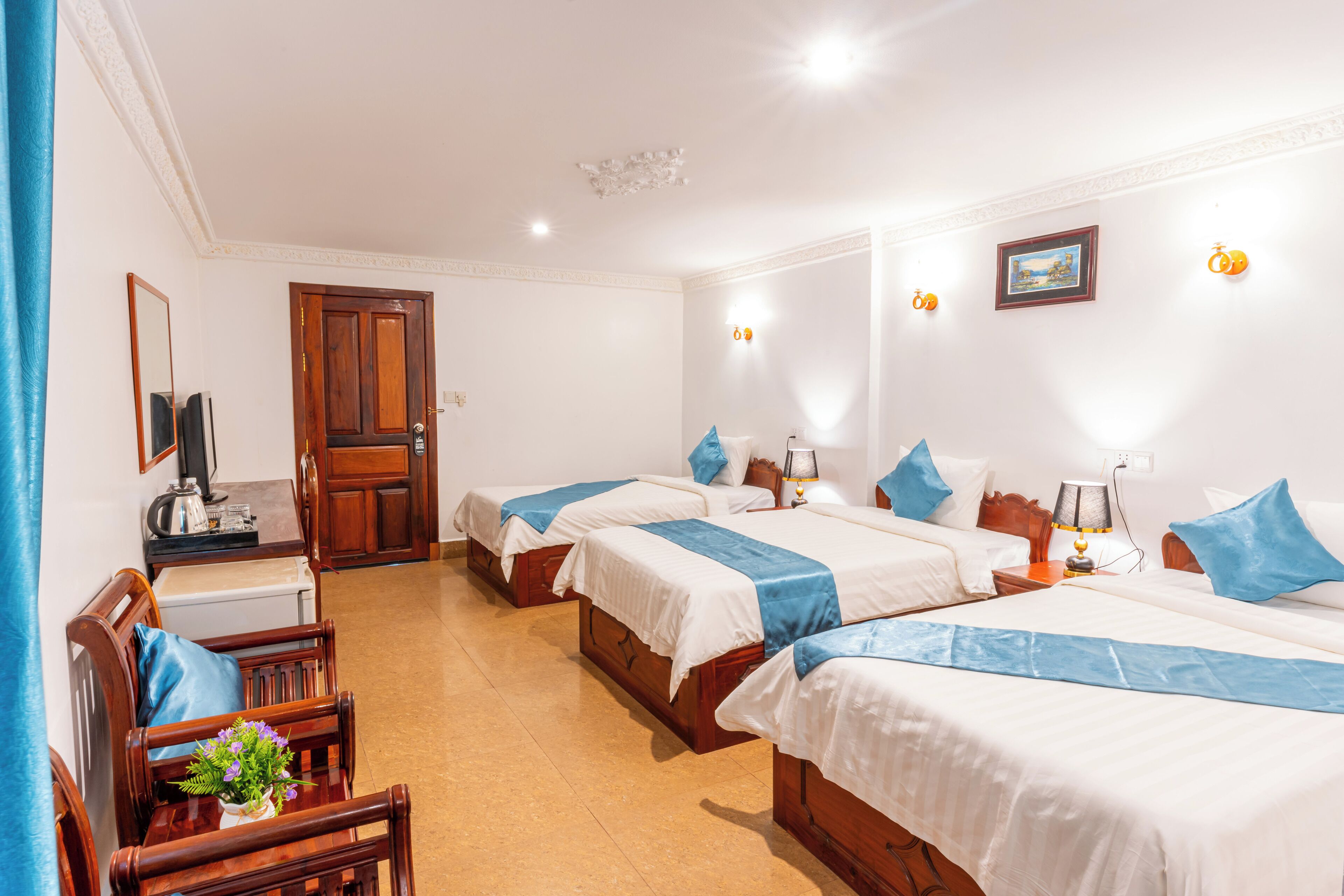 Une chambre d’hôtel avec quatre lits simples, un bureau en bois avec une chaise, une télévision et une porte donnant sur une autre chambre.