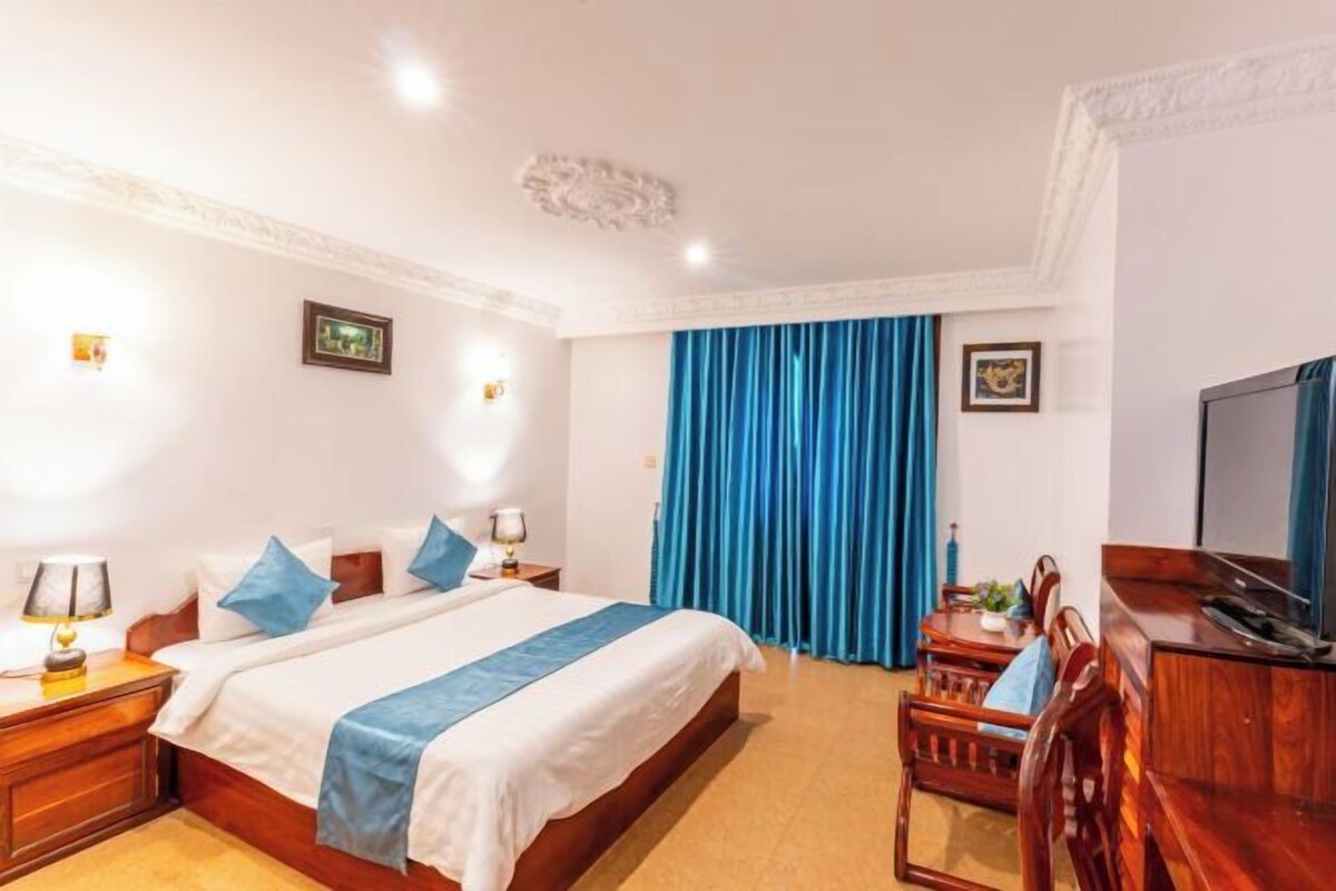 Une chambre d’hôtel avec un lit, des tables de chevet, un bureau, une chaise, une télévision et des rideaux bleus.
