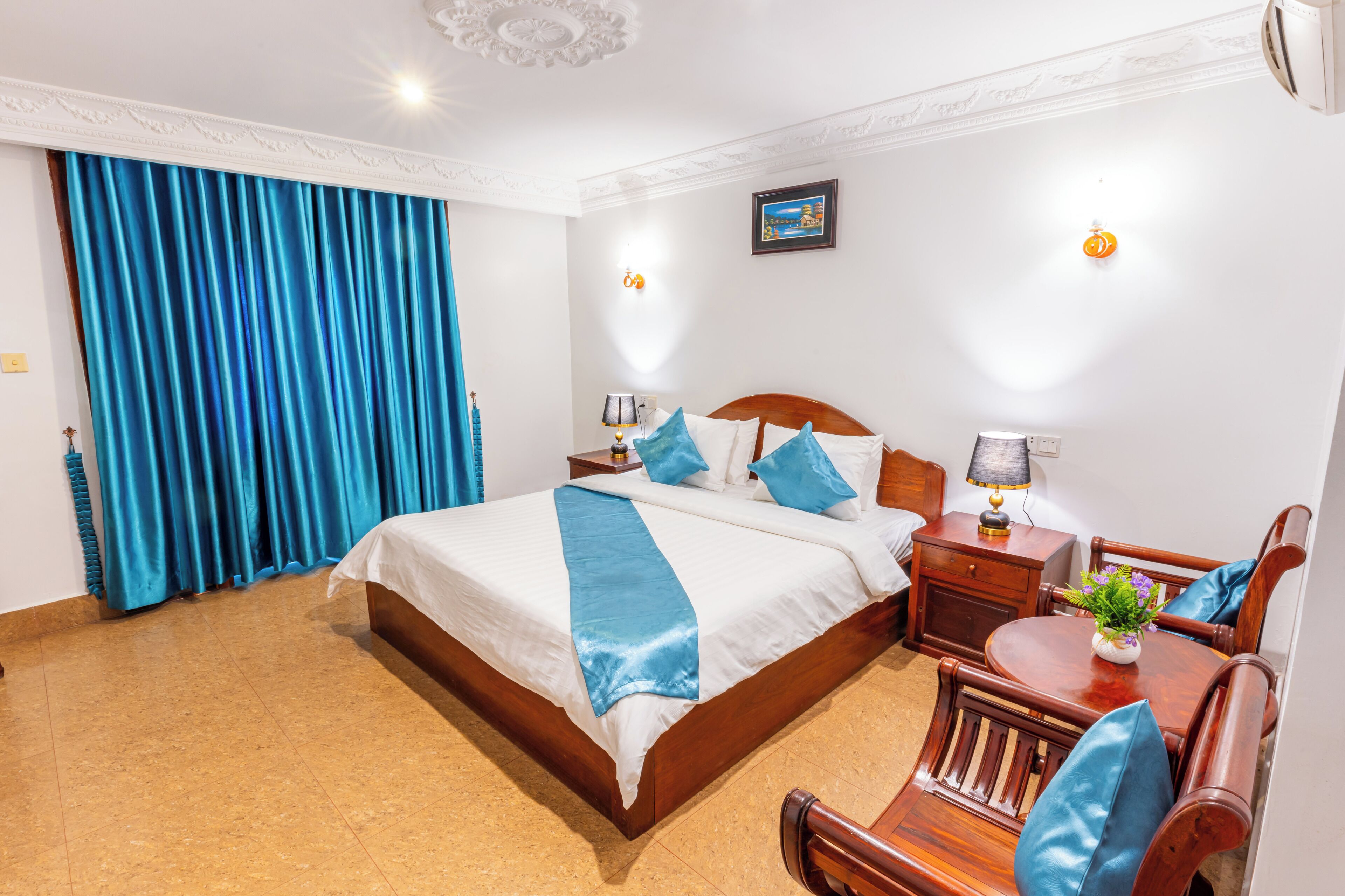 A hotel room with a large bed, a wooden nightstand, a desk with a chair, and a dining table.