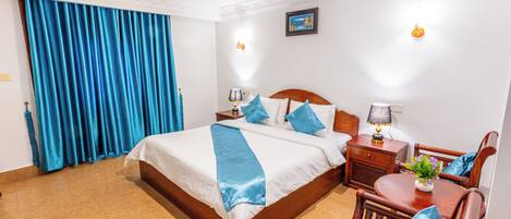 A hotel room with a large bed, a wooden nightstand, a desk with a chair, and a dining table.