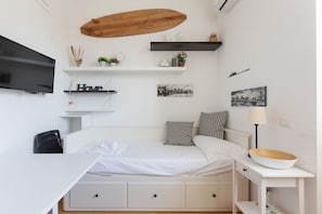 A bedroom with a bed, a desk, a TV, and wall-mounted shelves with decorative items.