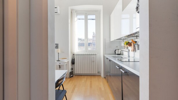 Et moderne køkken med et vindue, hvide skabe og et spiseområde med en stol.