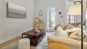 Un salon avec un grand tableau représentant une scène de plage, une table basse en bois, un canapé et une lampe.
