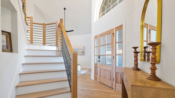 Un escalier avec des marches en bois et une rampe en verre, menant à une pièce dotée d’une porte en bois et d’un grand miroir.