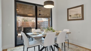 Un coin repas avec une table dressée pour quatre personnes, des chaises blanches, une plante en pot et un ventilateur de plafond.