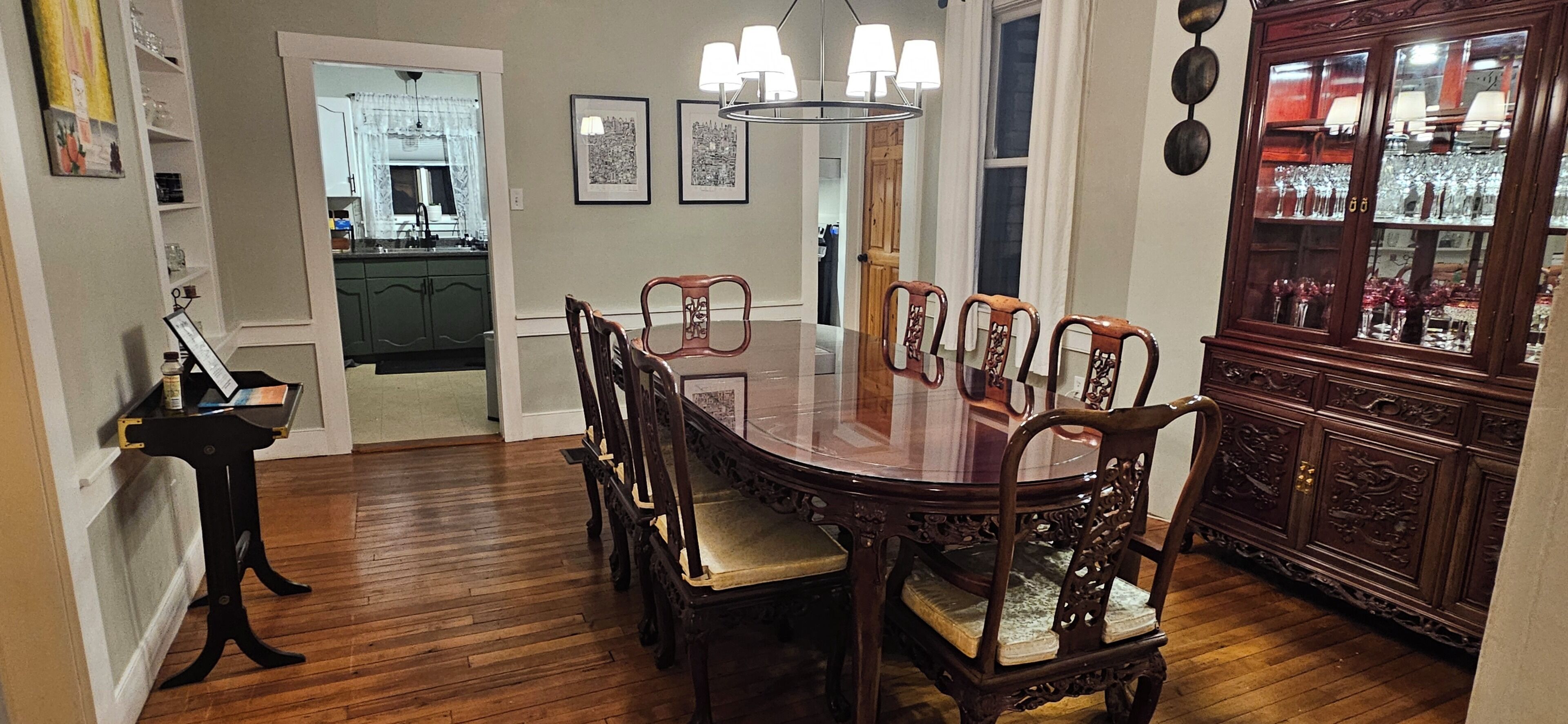 A dining area with a wooden table surrounded by chairs, a cabinet with glass doors, and framed pictures on the wall.