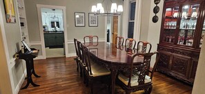 A dining area with a wooden table surrounded by chairs, a cabinet with glass doors, and framed pictures on the wall.