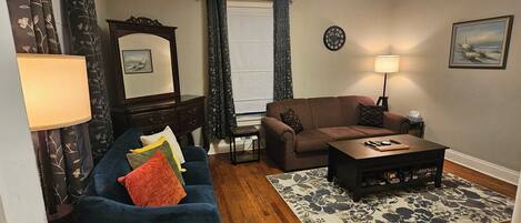 A living room with a sofa, a coffee table, a lamp, a clock, and a painting on the wall.