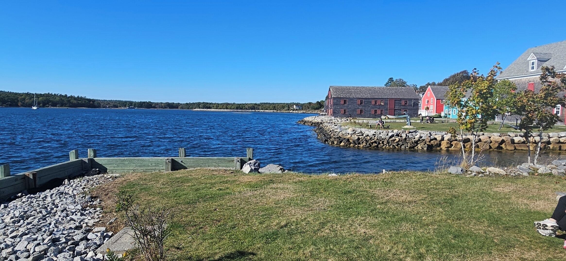 A waterfront property with a stone pier, a grassy area, and a red building with a grey roof.
