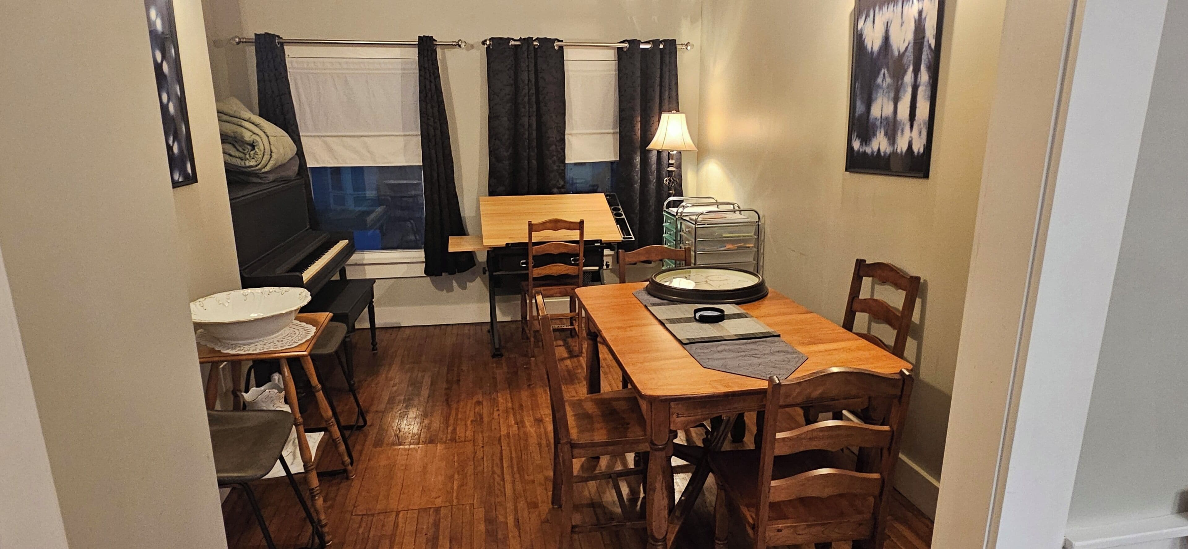 Een gezellig eetgedeelte met een piano, een tafel, stoelen, een lamp en een raam met gordijnen.