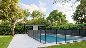 A swimming pool with a black fence, surrounded by a grassy area and trees. - Bonita Ranch (Miami Shores)