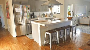 A modern kitchen with stainless steel appliances, a central island with stools, and a large window providing natural light. - Bonita Ranch (Miami Shores)