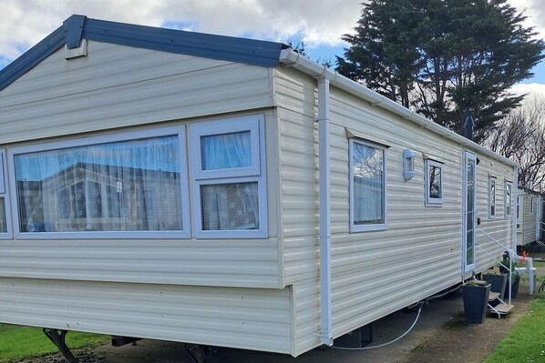 A mobile home with a gable roof, multiple windows, and a small porch area. - 3 Bed Caravan - Sleeps 8 - Pets - Parking - Wifi (Rhyl)