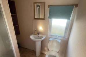 A small bathroom with a white sink, a mirror, and a toilet. - 3 Bed Caravan - Sleeps 8 - Pets - Parking - Wifi (Rhyl)